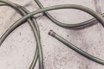 Tuyau vert enroulé sur béton, embout détaché, posé au sol