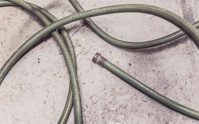 Tuyau vert enroulé sur béton, embout détaché, posé au sol